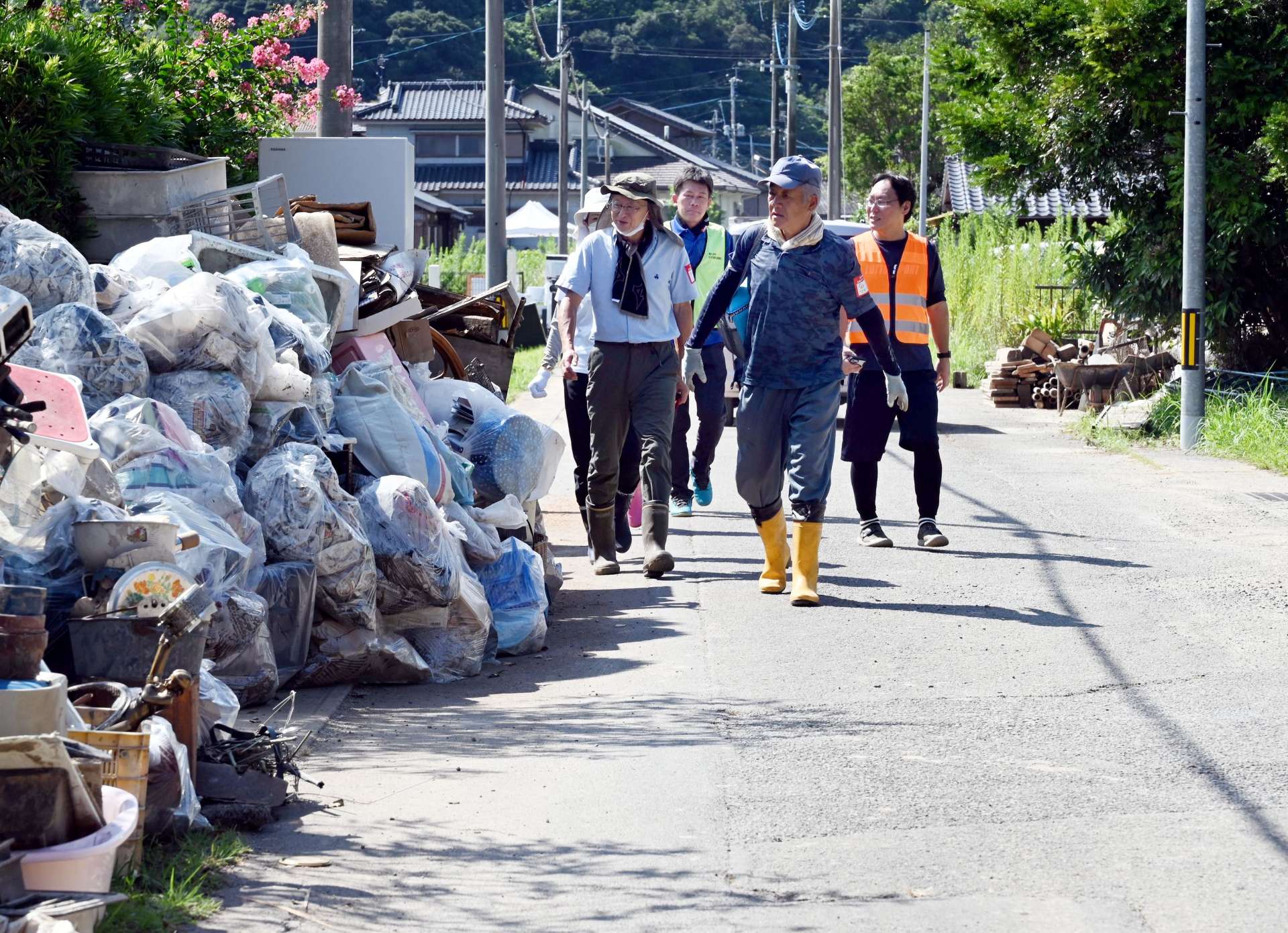 災害ごみが積まれた道路を歩き、活動場所へ向かうボランティア＝２８日、南さつま市加世田内山田