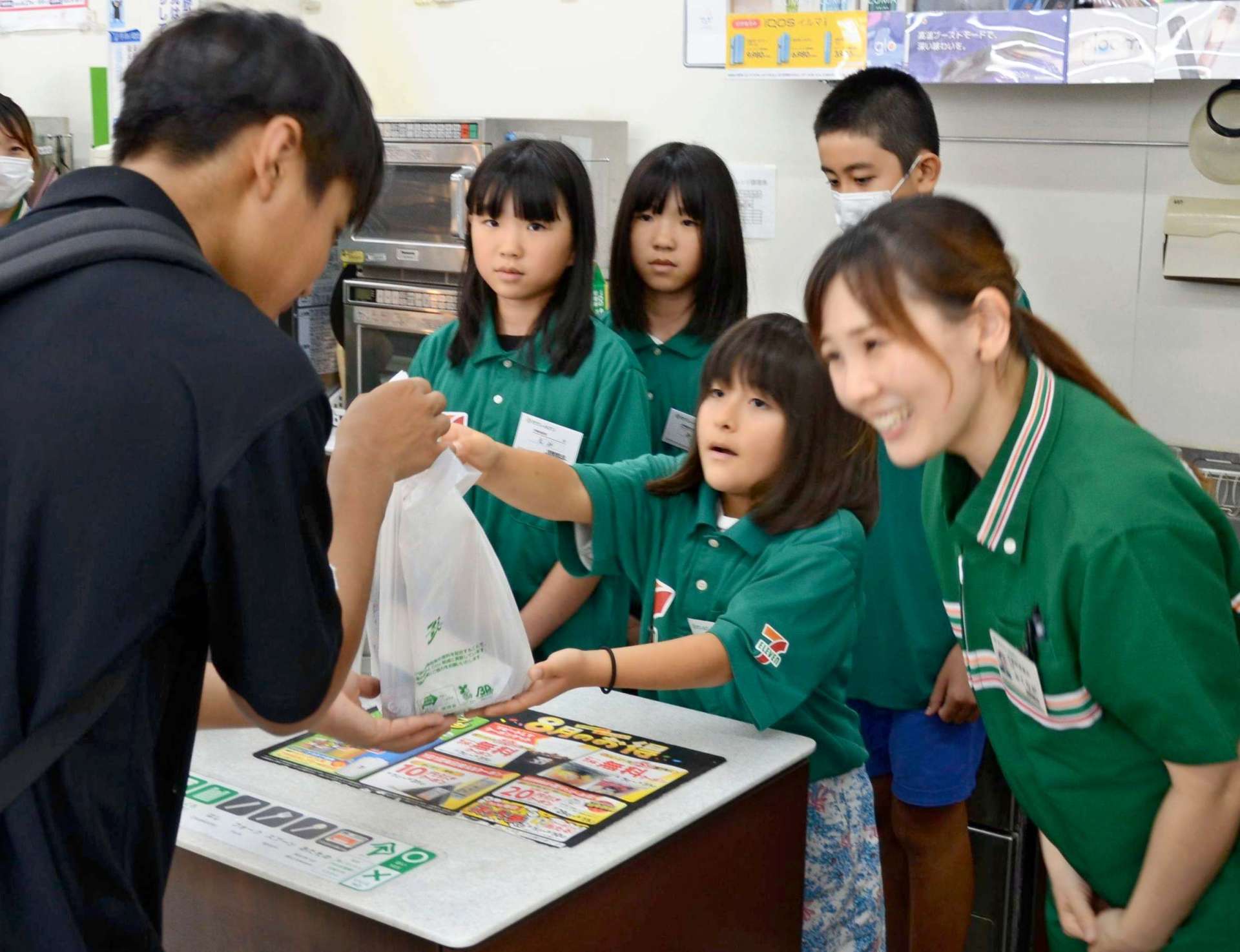 商品を渡し、接客する子どもたち＝日置市伊集院のセブン－イレブン伊集院徳重店