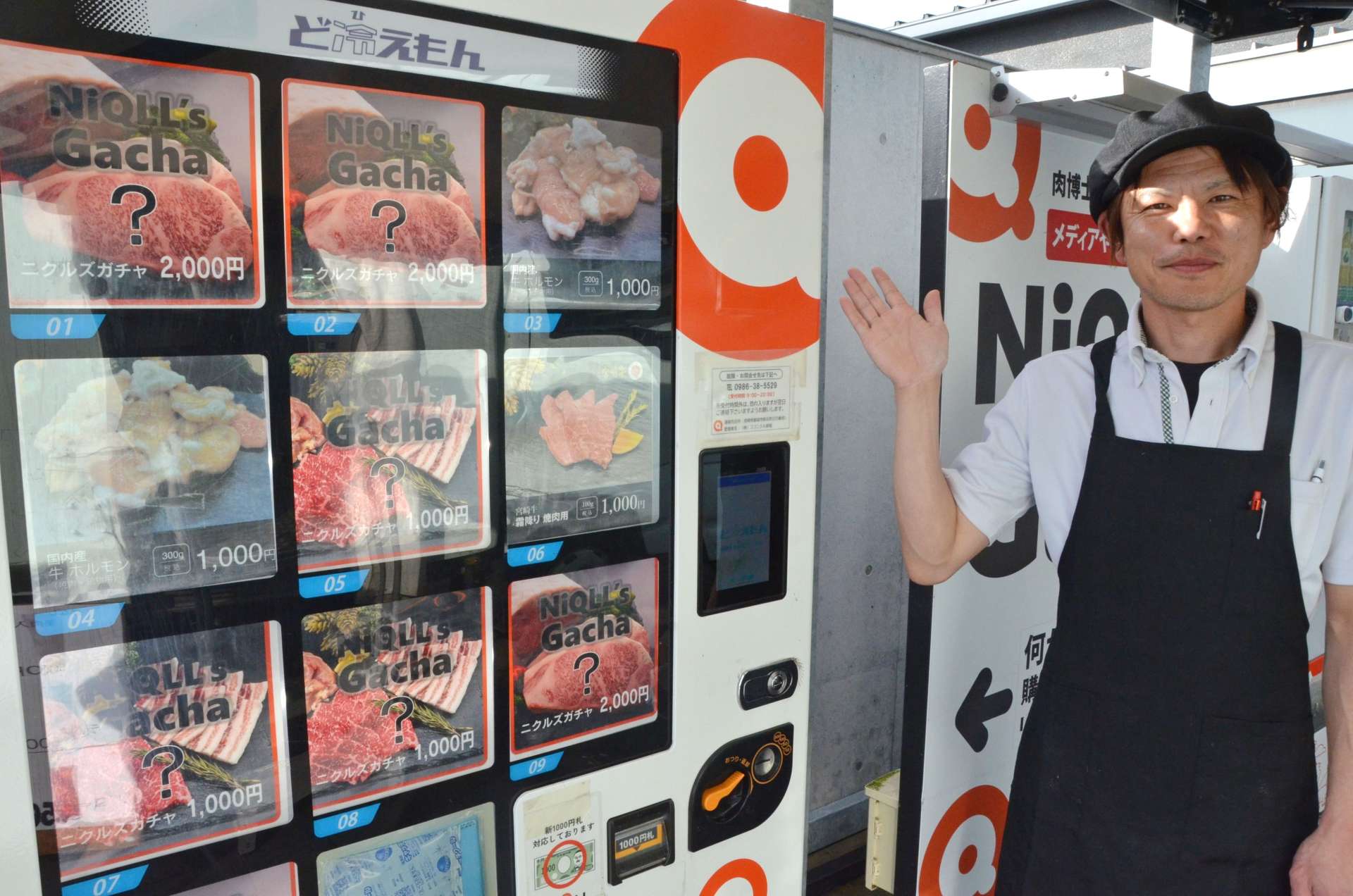 設置以来の売上高が１億円を突破した「ニクルズガチャ」とココニクル都城直販課の蕨野友樹さん＝都城市都北町