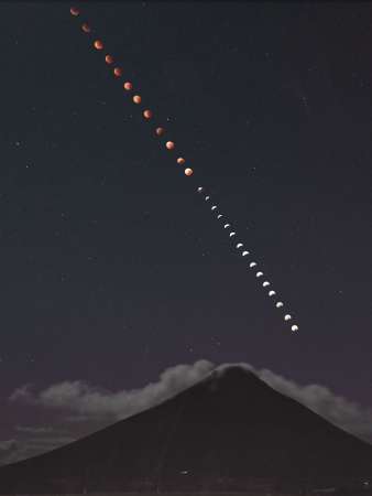開聞岳上空で雲に見え隠れしながら赤く染まった月＝８日、指宿市山川大山（午前２時５１分から２８枚を比較明合成）