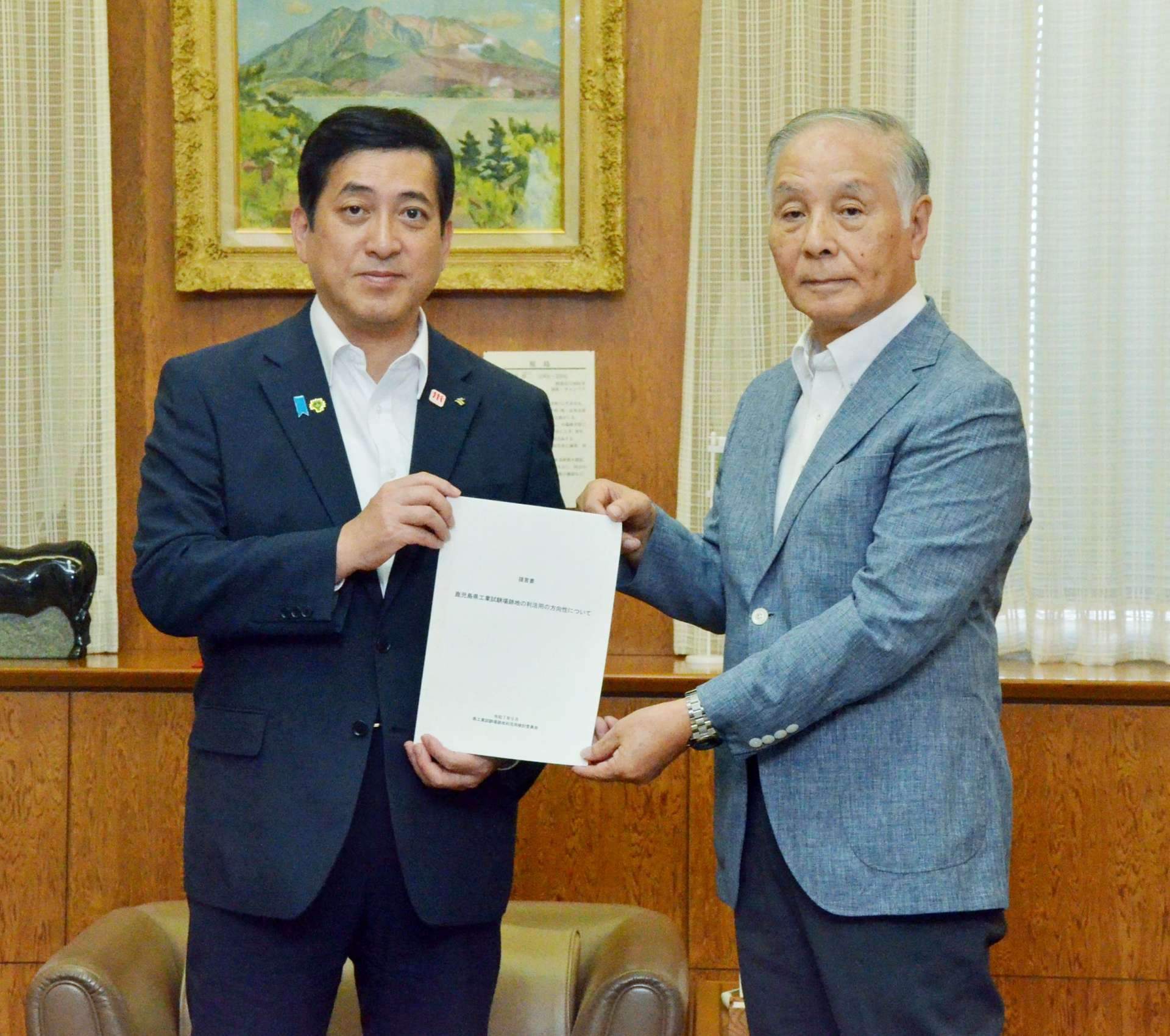 塩田康一知事（左）に県工業試験場跡地の利活用に関する提言書を手渡した検討委員会の井上佳朗委員長＝８日、県庁