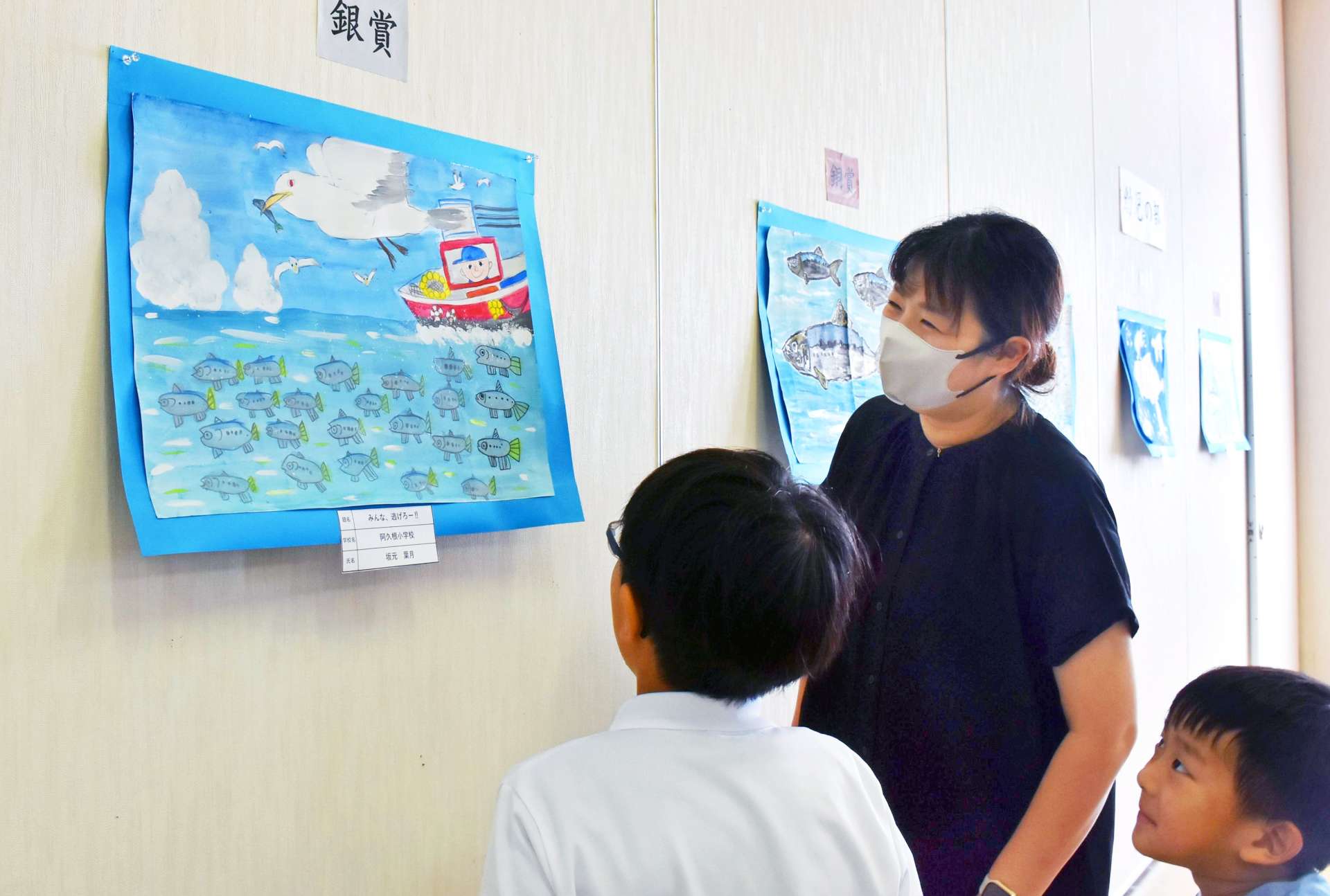 イワシ絵画コンクールの入選作を眺める親子＝阿久根市の北さつま漁協