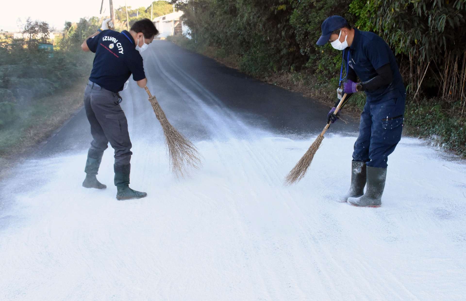 道路にまいた消石灰をほうきで均等にする出水市職員＝７日午後、同市荘