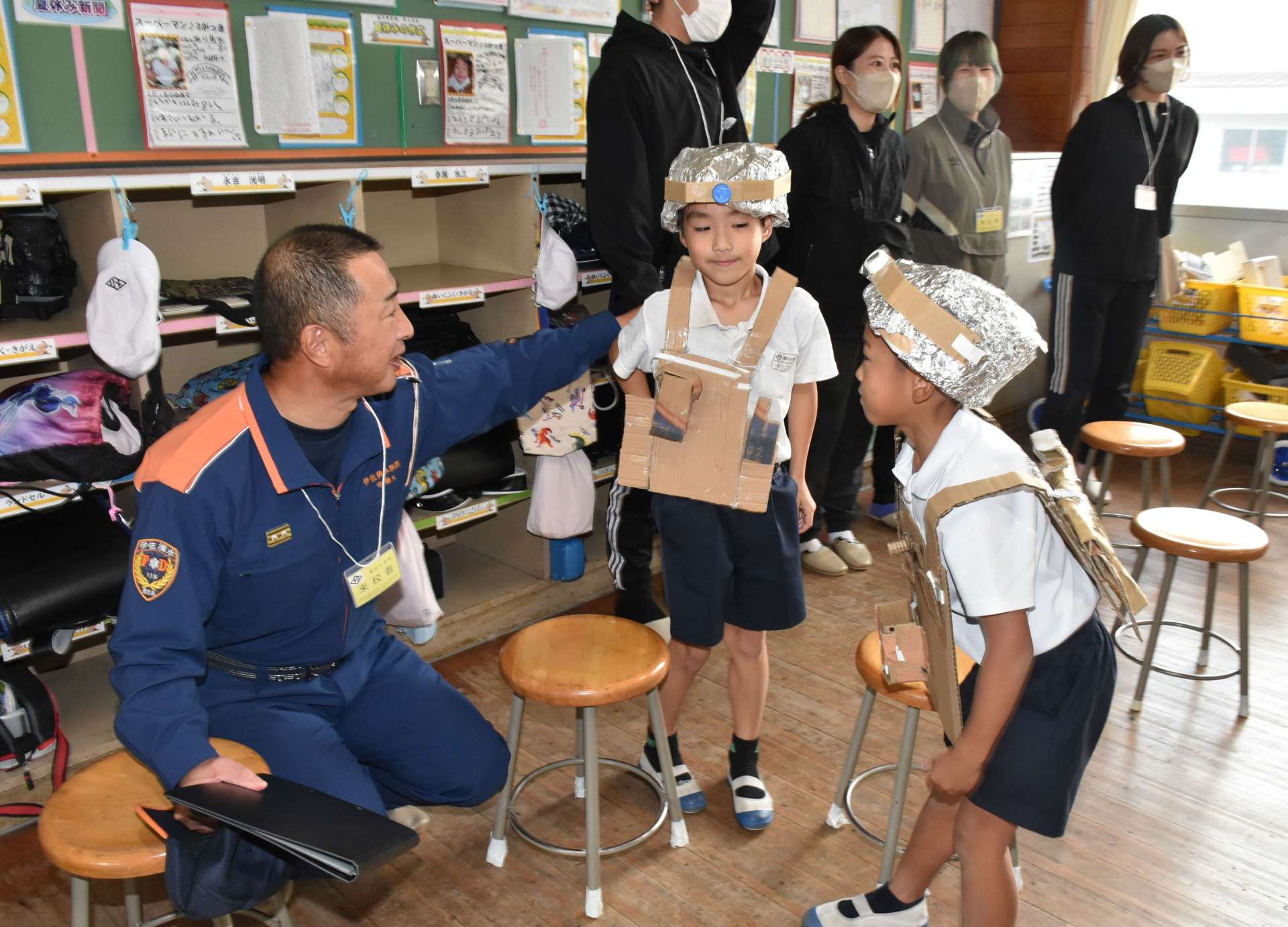 見学した菱刈分遣所の中島大陽所長（左）に自作の消防服、ヘルメットを見せる児童ら＝伊佐市の菱刈小学校