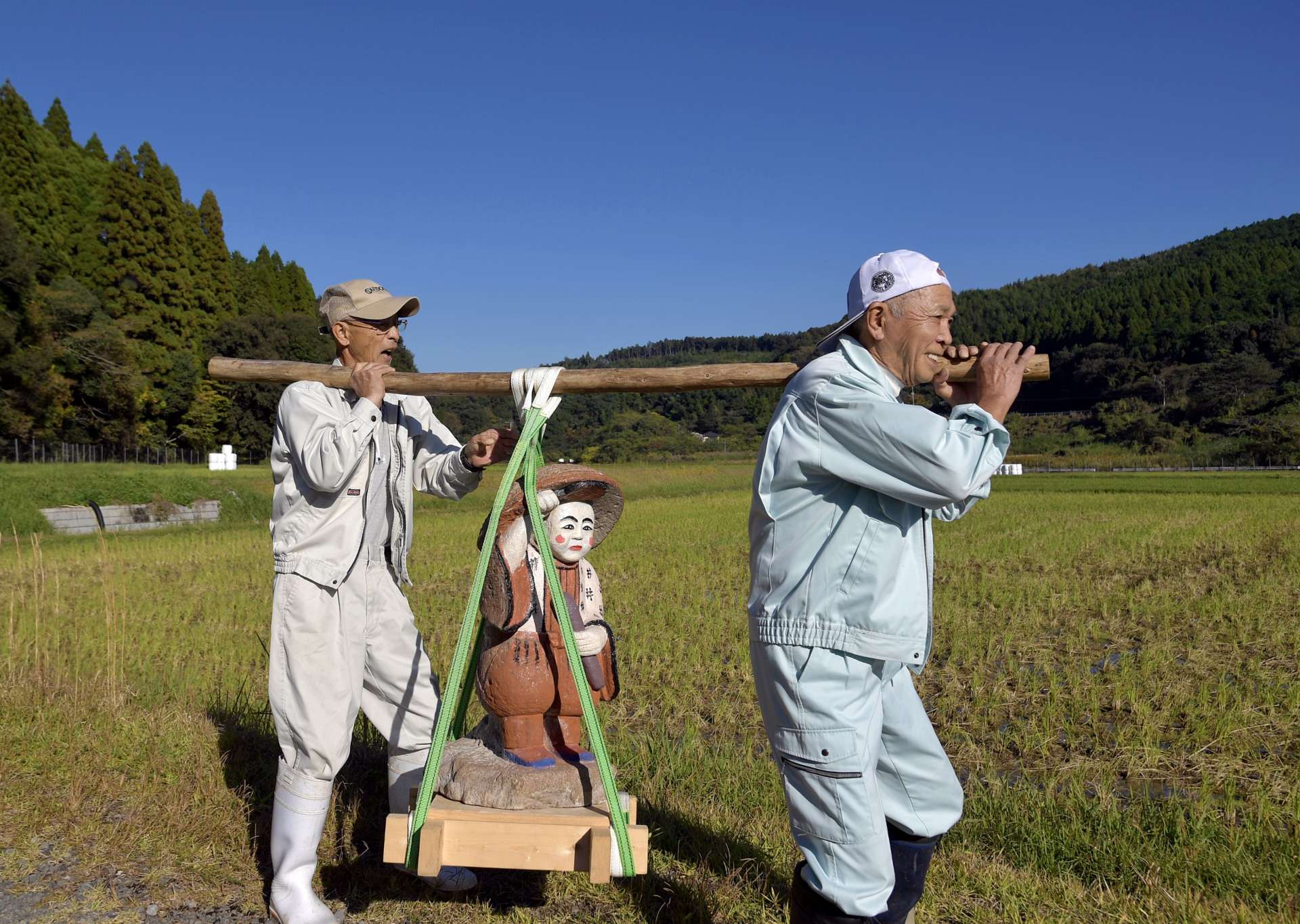 青く澄んだ秋空の下、下狩宿の住民に担がれ田んぼを見回る田の神＝１４日、さつま町求名