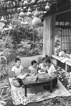 昭和37年8月、鹿児島市内。友だちを集め、縁側や庭で宿題の整理に大わらわの子どもたち。「ひょうたん棚を吹き抜ける風は、もう秋の気配」と当時の紙面。