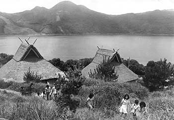昭和49年、旧山川町の鰻池湖畔。「夏草の生い茂った湖畔に五棟の弥生式小屋が建っている。青少年研修会が『青少年に自然との交流の場を』と建設した訓練棟である。四季を通じて若者たちでにぎわっている」と当時の紙面で取り上げている。