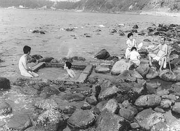 昭和37年、旧山川町山川港の天然露天ぶろ。「満潮時には海面下にかくれるから、そうじの必要もなく、干潮をねらって大自然の中にゆったり体をひたす。後ろは高いガケなので、のぞかれる心配もなく、全くのハダカ天国」と当時の紙面。
