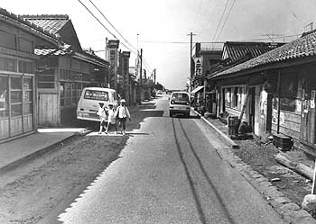 昭和49年、旧笠沙町小浦の商店通り。「商店街にしばらく待ち構えてみても、日中は買い物客がほとんど通らない。商店経営が容易でないことを如実に物語る。活路を求めるとすれば釣り観光の振興と、大浦干拓への企業誘致か」と過疎問題を取り上げている。