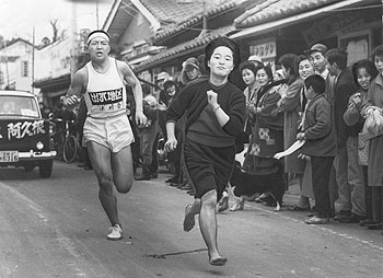 第4日8区、大崎町を力走する浦選手（出水）と、飛び出して伴走する女性＝昭和37年2月27日（現在、選手への伴走応援はできません）