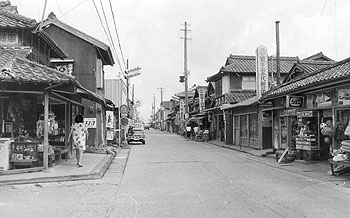 昭和49年、旧東郷町の商店街。「道幅が狭く車の離合がやっとで歩道もない。建設省が国道のバイパス建設を打ち出したが地元商工会は従来線の拡幅が先決と反対し、『バイパスか拡幅か』で工事は大幅に遅れている」と当時の紙面で伝えている。