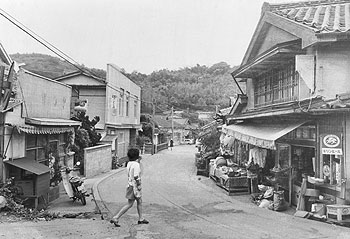 昭和49年、長島町の指江商店街。同年4月、黒之瀬戸大橋が開通し、「ただでさえ弱い購買力は交通の便がよくなったとたんに島外へ流れ、地元商店などは大型の資本と太刀打ちしなければならなくなった」と、経済情勢の厳しさを伝えている。