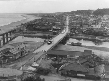 昭和３７年１２月、旧志布志町の権現橋と重要幹線道路。紙面によると、重要幹線工事は２６年着工。「千軒近い家屋の移転などの難事業を伴って十年の歳月を費やしたが、この夏完成した」と報じている