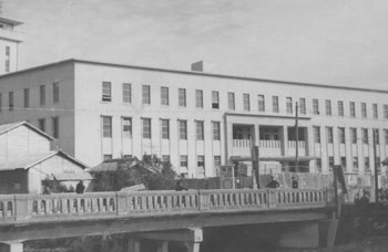昭和２６年１２月、旧鹿屋市役所。紙面は「市役所は鉄筋３階建てで外部は白色、入口はムラサキ、内部はタマゴ色のモダンな建築。十五日に落成式を挙げることになった」と報じている。