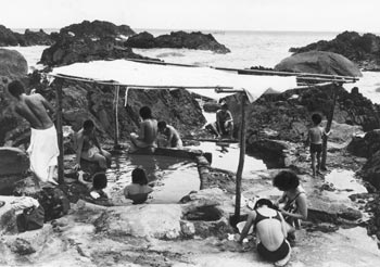 昭和４８年７月、夏休みの観光客らでにぎわう海中温泉。紙面によると「ゴツゴツした岩に囲まれ、満潮になれば海水がかぶる温泉。平内区が簡単な雨よけをつくって管理しているが、夏休みに入って地元の湯治客に加えて、島外から訪れた家族連れや若者が入れ代わり絶景の温泉を楽しんでいる」と伝えている。