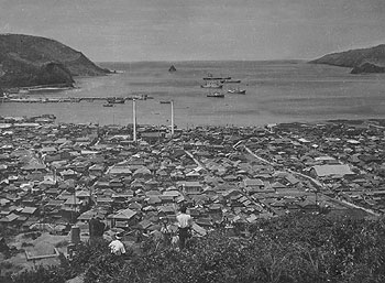 昭和２７年１０月、翌年１２月に本土復帰が決まった奄美大島、旧名瀬市街地の全景。当時の紙面は「戦災復興は進み、すでに人口は戦前を上回る３万３０００人。市街地にはモダンな鉄筋造りの郵便局や図書館なども整備された。また映画館やダンスホール、飲食店などもにぎわいをみせているという。一方、島民の生活の糧のひとつ、紬（つむぎ）業は最近、輸出手続きが緩和され、活発になってきた」と伝えている。