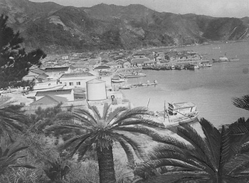 昭和３０年１２月２日、奄美大島南部の漁業基地として注目される古仁屋港。紙面では「かつては日本軍の要港で、本土防衛の前線基地だった古仁屋は今、瀬戸内４町村の中心地として、また漁業基地として重要視されている。港湾建設も急ピッチで、また大島海峡をむすぶ船便が十数隻、買い出し客らをのせて行き来する」と報じている。