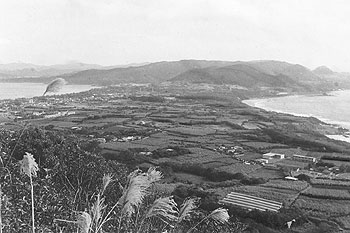 昭和６１年１２月、太平洋と東シナ海を一望する景勝地、龍郷町加世間（かしけん）の山手からの景観。紙面によると「赤尾木湾が陸に入り込み、くびれたように見渡せる。笠利方面の丘陵があたかも奄美の『ダイヤモンドヘッド』のよう。米統治時代には軍政官が『世界的な景観』と言ったのもうなずける」などと紹介している。