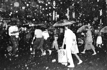 昭和６０年７月２９日、鹿児島市の中心街でバラバラと音をたてて降る桜島のドカ灰。紙面によると「桜島の噴火活動は８日連続して鹿児島市にドカ灰をもたらした。夜に入っても、市街地天文館に『ザーッ』と音をたてさながら雪のように降り、火山灰特有の硫黄臭が漂った。道行く人は傘をさし、ハンカチやタオルで顔を覆い、あわててアーケードに避難していた」と伝えている。