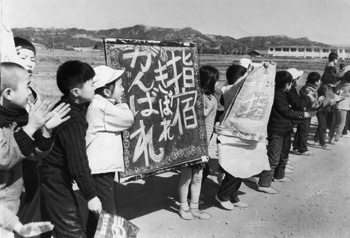 昭和４３年２月１９日、力走する選手にかわいい声援を送る山川町の大成小学校児童ら。当時のグラフ特集紙面によると「出場の選手が激しくせり合えば、沿道では応援合戦。鼓笛隊やのぼり、黒板までくり出して『がんばれ、きばれ』と駅伝気分は高まる一方だ。（中略）くふうこらして“紙芝居”式応援『指宿きばれ』と大成小の児童も声援」。