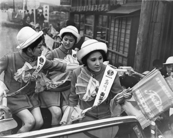 昭和４４年２月１６日、駅伝コース沿道に集まった応援の人々にＣＭガールが応援旗を配布。当時のグラフ特集紙面に「第１６回県下一周駅伝第１日は鹿児島－加世田の１１区、１３３．５キロで行われた。（中略）レースは各チームとも浮沈が激しく，上位下位でデッドヒートが繰り広げられた。先導車で沿道の地区民に応援旗を配るＣＭガール」などと紹介されている。