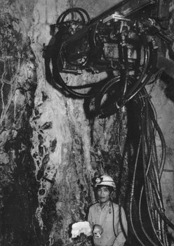 昭和６０年１１月、菱刈鉱山が坑道内を公開、撮影された“世界一”の金鉱脈。当時の紙面では「金の平均含有量がトン当たり１６２グラム。世界一の金鉱脈といわれる菱刈鉱山が、初めて報道関係者に坑道内部が公開された。脈幅２．５メートルの特大金鉱脈は坑道口から１８０メートル直下。黒っぽい緑色の凝灰岩の中を、滝のような白い太い帯が走っており、この金鉱脈に巨大な削岩機が突きささっていた」などと伝えている。