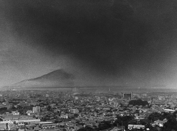 昭和４９年７月、降灰で真っ暗になった鹿児島市上空。紙面によると「２１日夜から２３日にかけて桜島が活発な活動を開始。これに伴って桜島南部、鹿児島市街地南部に大量の灰を降らせた。除灰車、グレーダーと合わせて３台で除灰作業に当たったが、除いても除いても降りつもる灰に、運転手たちもがっかりした表情」と当時の様子を伝えている。