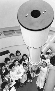 昭和４４年６月、県教育センターで２０センチの天体望遠鏡で天体観測する先生たち。紙面によると「県が吉田村（現鹿児島市）に総工費４億１５００万円をかけて建設した教育センターは超デラックス版。各地から“勉強する教師たち”がつめかけ、泊まりこみでカンづめ研修をうけている」と伝えている。