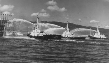 昭和４４年９月、喜入町（現鹿児島市）の喜入原油基地で放水するタグボート。紙面によると「７日後の大型タンカー第１船『かいもん丸』基地入りを控え、油火災を想定した防災訓練が行われた。タグボート自慢のドイツ式キャノン砲の消火銃が化学消火剤を混ぜた海水を１分間に３０００リットル放射、消火した」と報じている。
