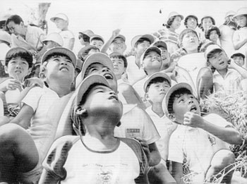 昭和５０年９月９日、宇宙開発事業団が打ち上げＮロケットを追う小学生。紙面は「オレンジ色の炎、立ちこめる白い煙、腹に響くごう音－日本最大のＮロケットは発射された。垂直にのぼってゆく真っ白い機体は、上空約１０００メートルあたりで、白く細い航跡を残して、真っ青な南国の空に消えていった。ロケット打ち上げの成功に町中がよろこびに沸いた」と伝えている。