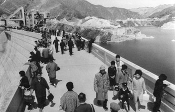 昭和４０年４月、完成し見物客でにぎわう鶴田ダム。「地元民や、世紀の完工式をひと目みようと、鹿児島市から貸し切りバスでやってきた人が、早朝からダムサイトに詰め掛けた。式が済むと待ち構えていたようにえん堤の上に押し掛け、“西日本一”の威容を誇るダムに目を見張っていた」と紙面は報じている。