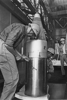 昭和４０年１１月、東京大学宇宙航空研究所が内之浦町（現肝付町）から打ち上げ予定のカッパ１０型１号機の整備点検。紙面は「同機は自動姿勢制御装置が内蔵され、ロケット本体を軌道に乗せるまでの実験を行う。テストが成功すれば、来春にも国産衛星第１号が内之浦から世界を雄飛する可能性が大きい」と伝えている。