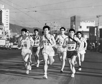 昭和４６年２月１３日、第１８回県下一周駅伝が開幕。市郡代表の１２チームと遠征２回目の沖縄チームが参加して行われた。写真は鹿児島市新屋敷町。