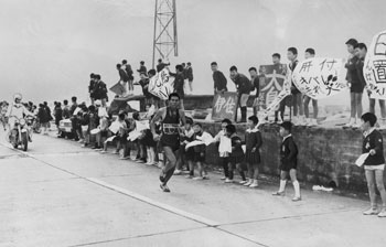 昭和４６年２月１７日、第１８回県下一周駅伝最終日。福山小児童の声援を受け、スパートする右田選手（鹿児島）。「沖縄と鹿児島の激しい優勝争いは、鹿児島が２分差を逆転し７年ぶり７回目の優勝で幕を下ろした」と紙面は伝えている。