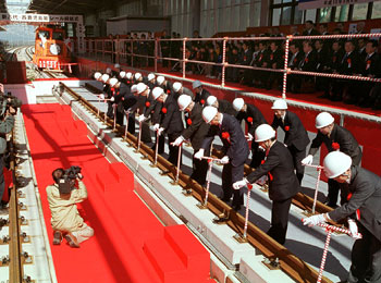 平成１５年３月、出水市の新幹線出水駅構内であった九州新幹線西鹿児島（現鹿児島中央）－八代間のレール締結式。紙面によると「関係者らが最後のレールをボルトで締めてコンクリート路盤を固定。同区間１２７．５キロのレールすべてがつながった」と報じている。
