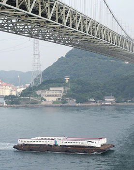 平成１５年８月、台船に載せられ関門海峡を通過する九州新幹線車両「つばめ」。「山口県から川内市の車両基地に海路向かう途中、九州の玄関口を通り抜けた。航路幅は最も狭いところで約５００メートル。多数の船舶が往来し、潮の流れも速い難所を、ゆっくりと慎重に進んだ」と紙面は報じている。