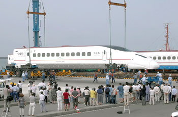 平成１５年８月、川内港に到着し陸揚げされる新幹線車両「つばめ」。紙面は「山口県から台船に載せて運ばれてきた第１編成６両（長さ２５メートル、重さ３０トン）を１両ずつクレーンでつり上げ、陸揚げ。港には鹿児島に"初上陸"した新幹線を一目見ようと、多くの家族連れらが訪れた」と伝えている。