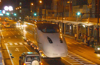 平成１５年８月、未明の川内市街地（現薩摩川内市）を抜け、車両基地へ向かう新幹線車両「つばめ」。紙面によると午前１時、最初の車両がトレーラーに固定されて川内港を出発。「約２１．５キロをパトカーや関係車両に誘導され、約２時間半かけて慎重に運んだ」という。