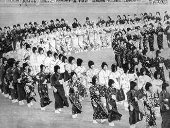昭和５３年１１月３日、名瀬市運動公園陸上競技場で県体開会式前に行われた奄美高生徒による集団演技「八月踊り」。紙面では「本土復帰２５周年を記念した第３２会県民体育大会は奄美大島を中心に開幕、開会式は約３万５０００人の選手団、観客が会場を埋めつくし、県体始まって以来の大がかりな大会となった。」と報じている。