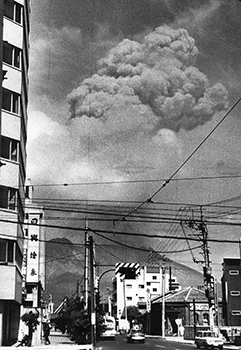 昭和４３年６月４日午後２時５５分、鹿児島市朝日通からの爆発した桜島。紙面では「最近にない大きな爆発を起こしたが、さいわい人畜に被害はなかった。しかし人頭大の赤熱噴石が山上を飛びかい、有村地区では４合目付近まで落石、５カ所で山火事が起こったのを確認。また、黒神町では爆発でタナのビンがくずれ落ち、戸外に飛び出す地区民が多かった。さらに黒神、有村付近一帯に落ちた噴石の砂じんが垂水市役所の屋上からもはっきり認められた」と報じている。