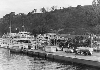 昭和４４年、改築工事を始める前の桜島袴腰港待ち合い所。紙面では「現在の待ち合い所は、戦前からの木造建築で、改造を重ねてきたが、狭くて観光客をさばききれないありさま。総合ターミナルの完成を待ってこれまでの待ち合い所をとり払い、団体客専用の貸し切りバスの発着場に利用する。さらに、園地をつくり、桜島に多いアコウノ木などを植え込んで南国ムードを盛りあげ、バスを待つ観光客のいこいの場にしたいという」と報じている。
