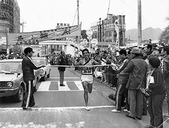 昭和５０年２月１８日、第２２回鹿児島県下一周駅伝第４日。鹿屋市役所前で笑顔で日間優勝のゴールをする肝付・島津選手。肝付は２日目の不振がうそのような奮闘ぶり。総合優勝を射程内にとらえ、川井田を初起用するなど闘志満々。日間優勝で鹿児島との差をさらに縮め最終日の決戦に持ち込んだ。