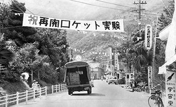 昭和４３年９月、内之浦町に久々にかかげられたロケット実験再開を祝う横断幕。９月１０日からの東大宇宙空間観測所ロケット実験再開を前に、地元内之浦町は中央通りに「祝・ロケット実験再開」の横断幕や万国旗が飾られ、ロケットムードが高まって実験を待つばかりとなった。