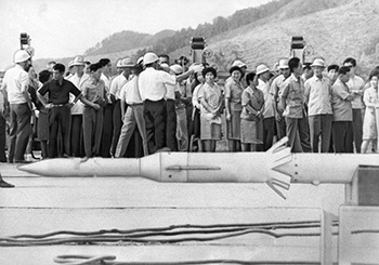 昭和４３年、１年５ヶ月ぶりのロケット実験再開を前に見学者でにぎわう内之浦の宇宙センター。再開前夜の９月９日は、町内の１２、３軒の旅館はほぼ満員、“ロケット景気”にわいた。７月見学客はおよそ１６６０人、８月にはおよそ２．５倍の４０００人にふくれ上がった。ほとんどが帰省客で、郷里に帰ったついでに、家族や友人をつれて見学に来たというグループが目立った。９月に入ると連日のように見学客が訪れ土、日曜日は１日に、２００人平均という盛況。