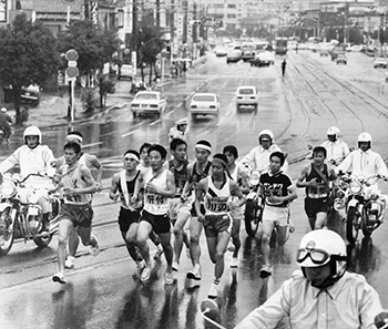 昭和５１年２月１４日、鹿児島市武之橋で一団となって力走する各チームの第１走者たち。第２３回鹿児島県下一周駅伝競走大会は県内１１チームが参加、雨のなか鹿児島市の南日本新聞社前をスタートした。大会には伊佐チームが出場を断念、フルエントリーとはならなかったが、県内２３１人の健脚がずらりそろった。