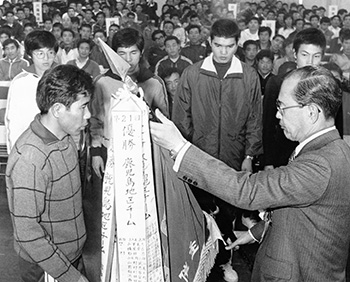 昭和５１年２月１８日、閉会式で大会優勝旗を受け取る右田・鹿児島チーム主将。５日間沿道の声援を受けて白熱のレースを展開した第２３回鹿児島県下一周市郡対抗駅伝競走大会は、鹿児島チームが４年連続１１回目の総合優勝をとげて大会の幕を閉じた。大会終了後、南日本新聞社６階ホールで閉会式があり、選手、役員ら約３００人が参加した。
