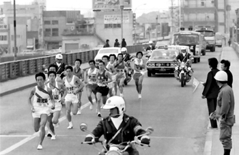 健脚は早春の北薩路へ。第２４回鹿児島県下市郡対抗駅伝３日目は昭和５２年２月１４日午前９時、川内市の川内警察署前から日当山のゴールをめざして一斉にスタート、いよいよ中盤戦に突入した。郷土入りを飾った川辺、出水のめざましい奮起、激しい首位争いで一段と見ごたえの盛り上がった大会だけに沿道は小、中学生の小旗がゆれ、地元・川薩チームはもちろん、遠来の大島、熊毛にも盛んな声援。伊佐チームの欠場といういちまつの寂しさはあるものの、大口市内でも歓迎の人波ができた。